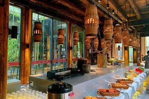 Une longue table de buffet garnie de divers plats, des poutres en bois et des luminaires suspendus dans une pièce spacieuse.