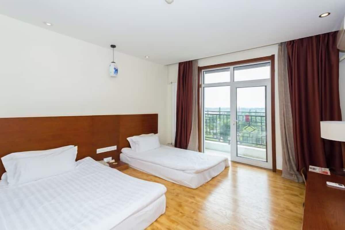A hotel room with two beds, a wooden headboard, a large window with curtains, and a view of the outside.