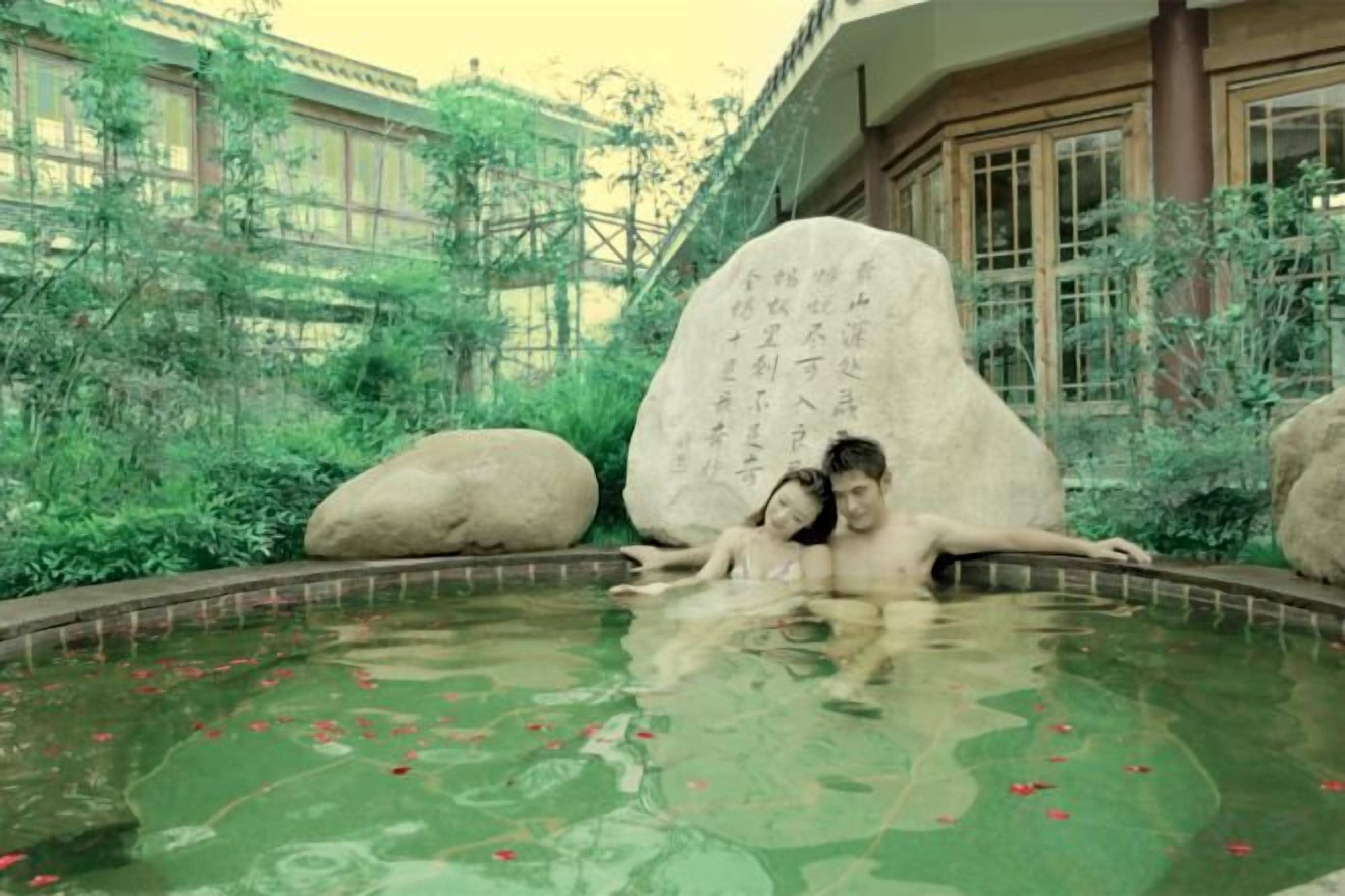 A couple in a hot spring with large rocks and Chinese calligraphy.