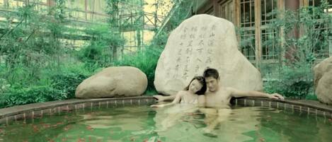 A couple in a hot spring with large rocks and Chinese calligraphy.