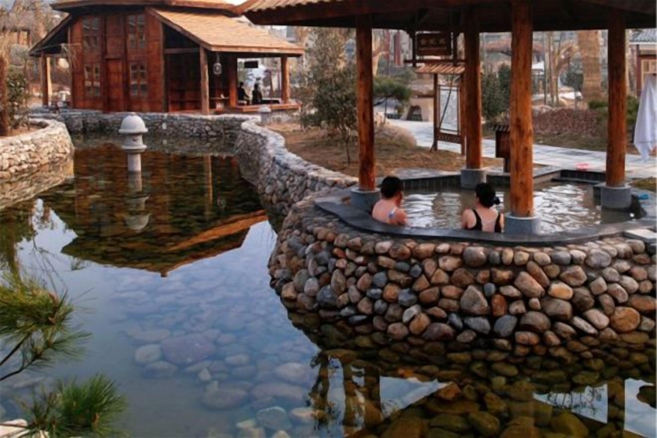 A hot spring area with a stone platform and a wooden pavilion.