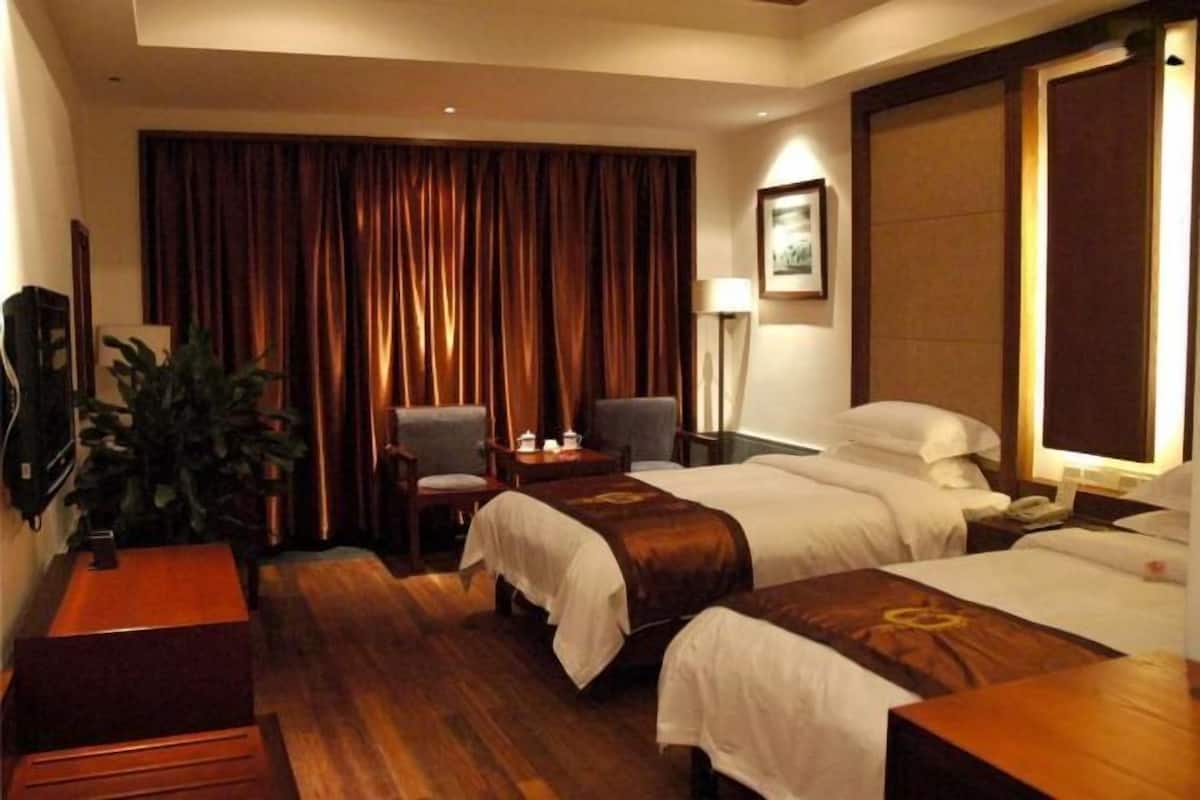 A hotel room with two beds, a desk, a chair, a lamp, and a large window with curtains.