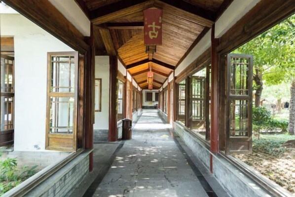 Un couloir aux poutres en bois et aux grandes fenêtres, qui mène à une porte au fond.