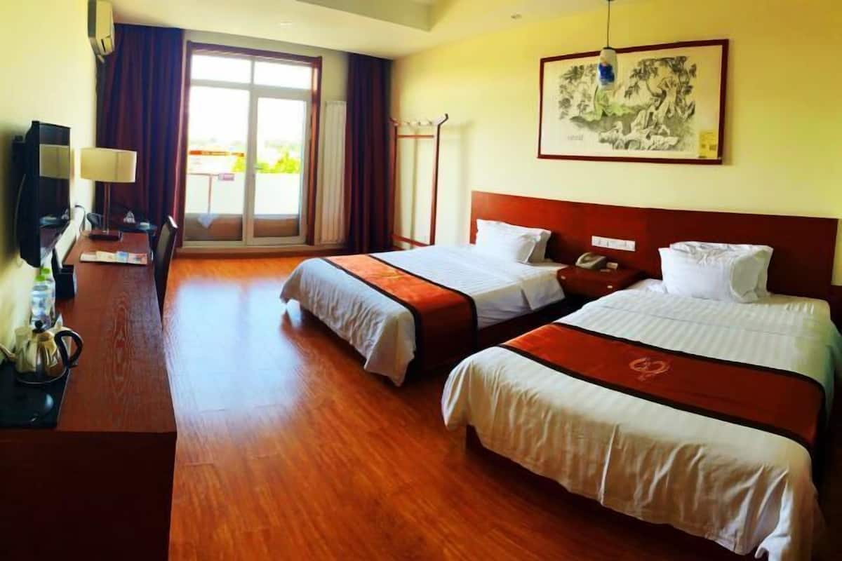 A hotel room with two beds, a desk with a lamp, a television, and a large window with curtains.