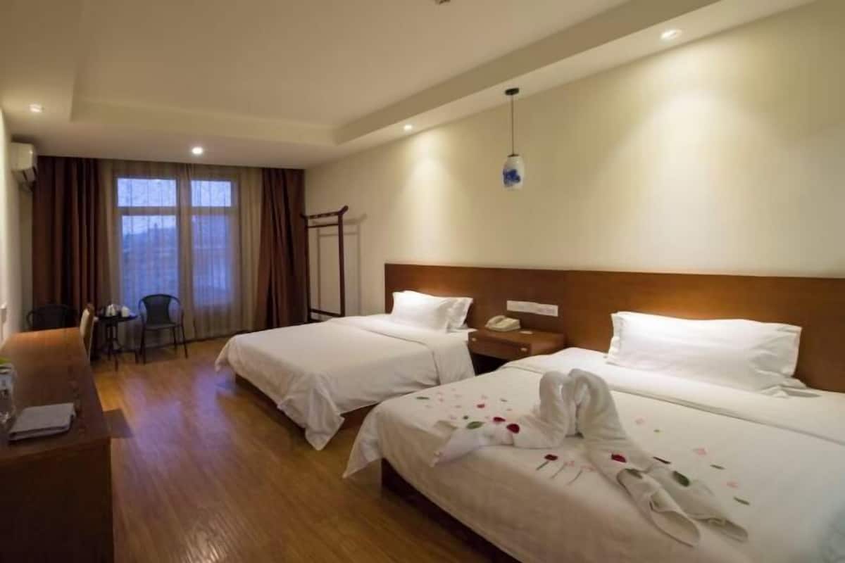 A hotel room with two beds, a desk, a chair, and a window with curtains.