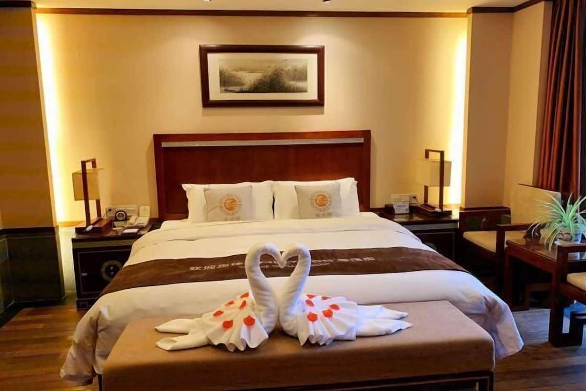 A hotel room with a large bed, a wooden headboard, a bedside table with a lamp, and a framed picture on the wall.