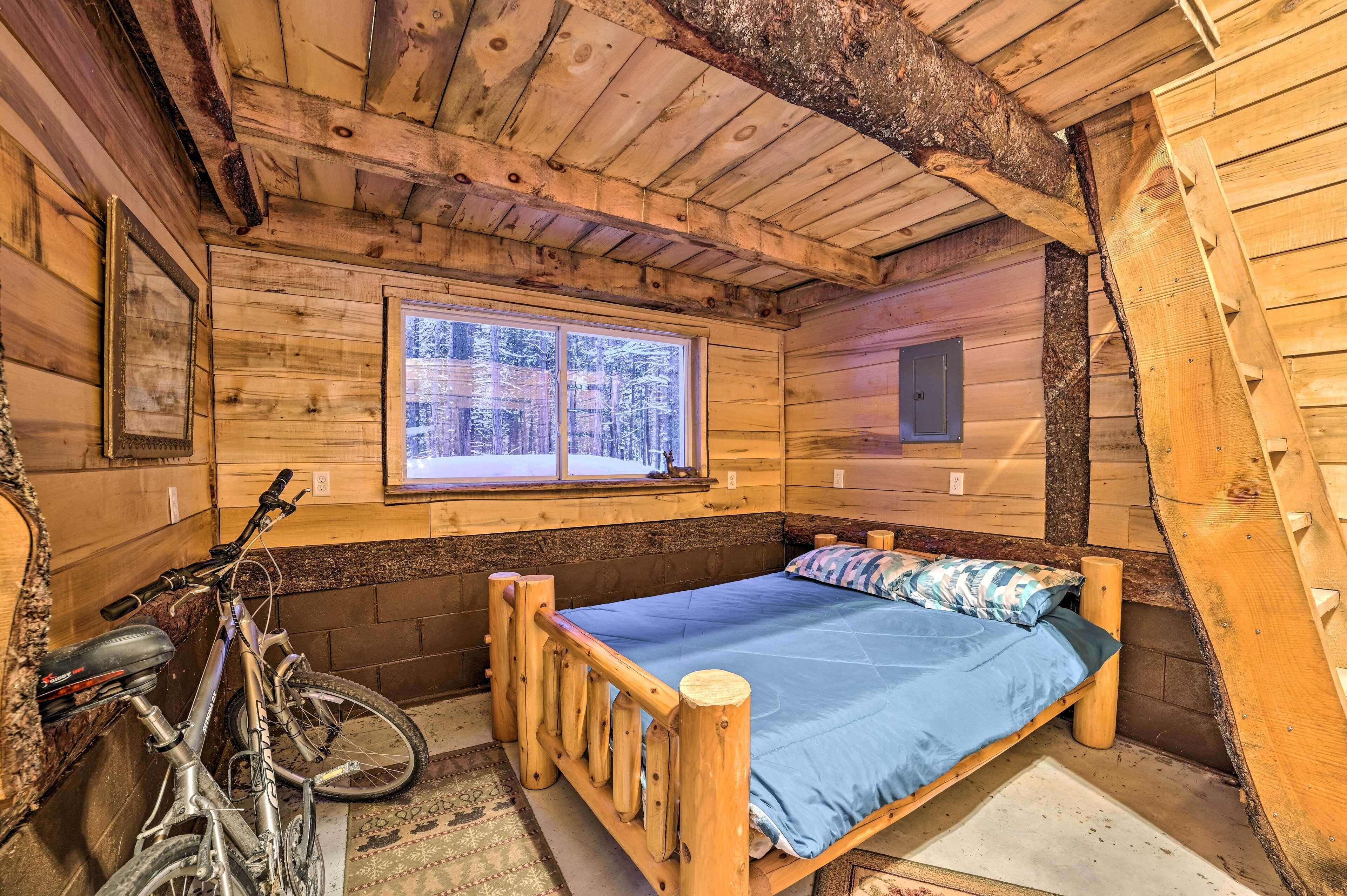 Habitació d'una cabana de fusta amb un llit, una finestra i una bicicleta.