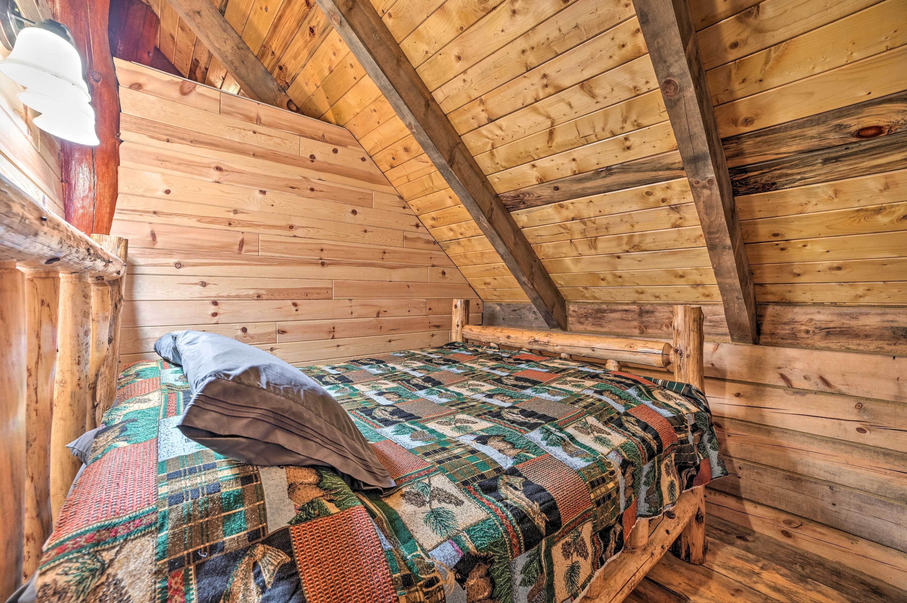 A wooden cabin room with a bed, a quilt, and a slanted ceiling.