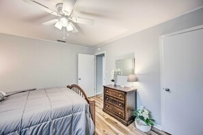 A bedroom with a bed, wooden dresser, ceiling fan, and a door leading to another room. - Longview Vacation Rental Home: 4 Mi to Dtwn (Longview)