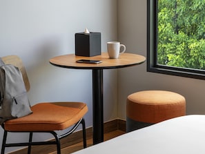 Une chambre d’hôtel avec une table ronde en bois, une tasse blanche, un smartphone et un objet noir posé sur la table.