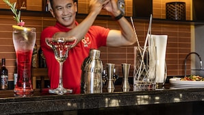 Um bartender preparando uma bebida em um bar, com diversos utensílios de bar e garrafas.