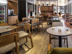Un restaurante moderno con mobiliario de madera, mesas redondas y diversas opciones de asientos.