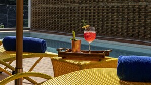 Área de piscina com cadeiras de vime amarelas, uma toalha azul e um copo com bebida vermelha e rodela de limão.