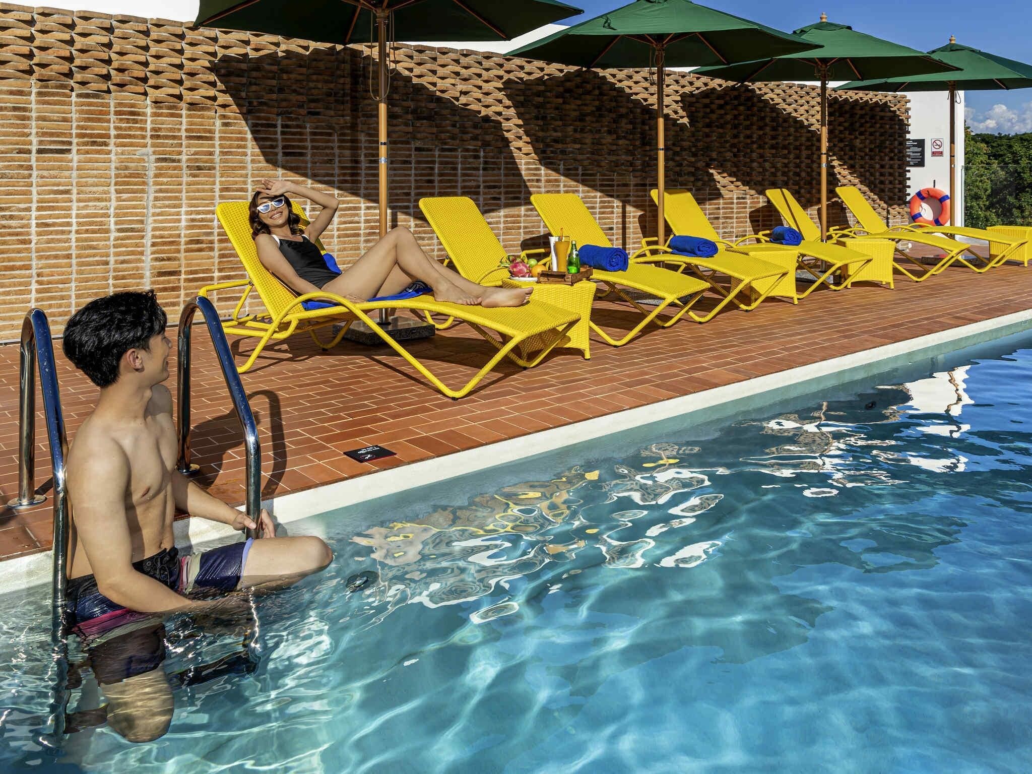 A swimming pool with yellow lounge chairs and a brick wall.