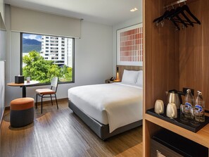 Habitación de hotel moderna con una cama grande, un escritorio, una silla y vistas a un paisaje urbano.