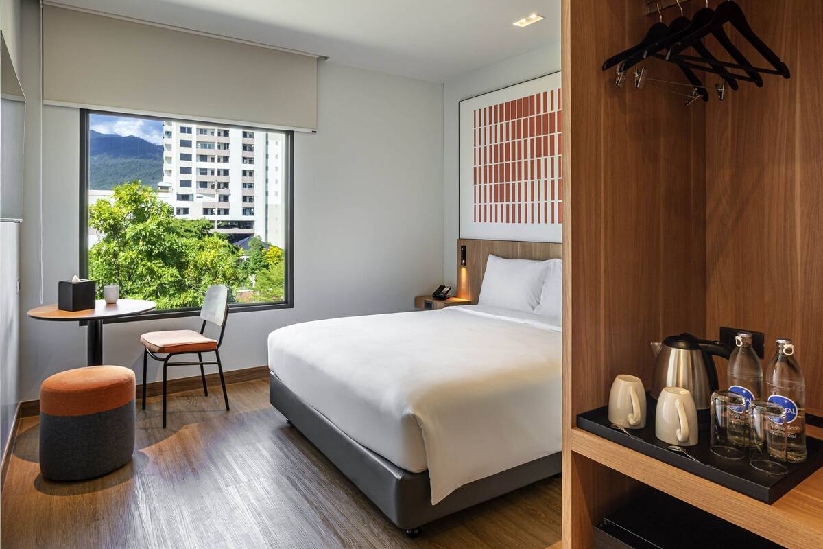 Habitación de hotel moderna con una cama grande, un escritorio, una silla y vistas a un paisaje urbano.