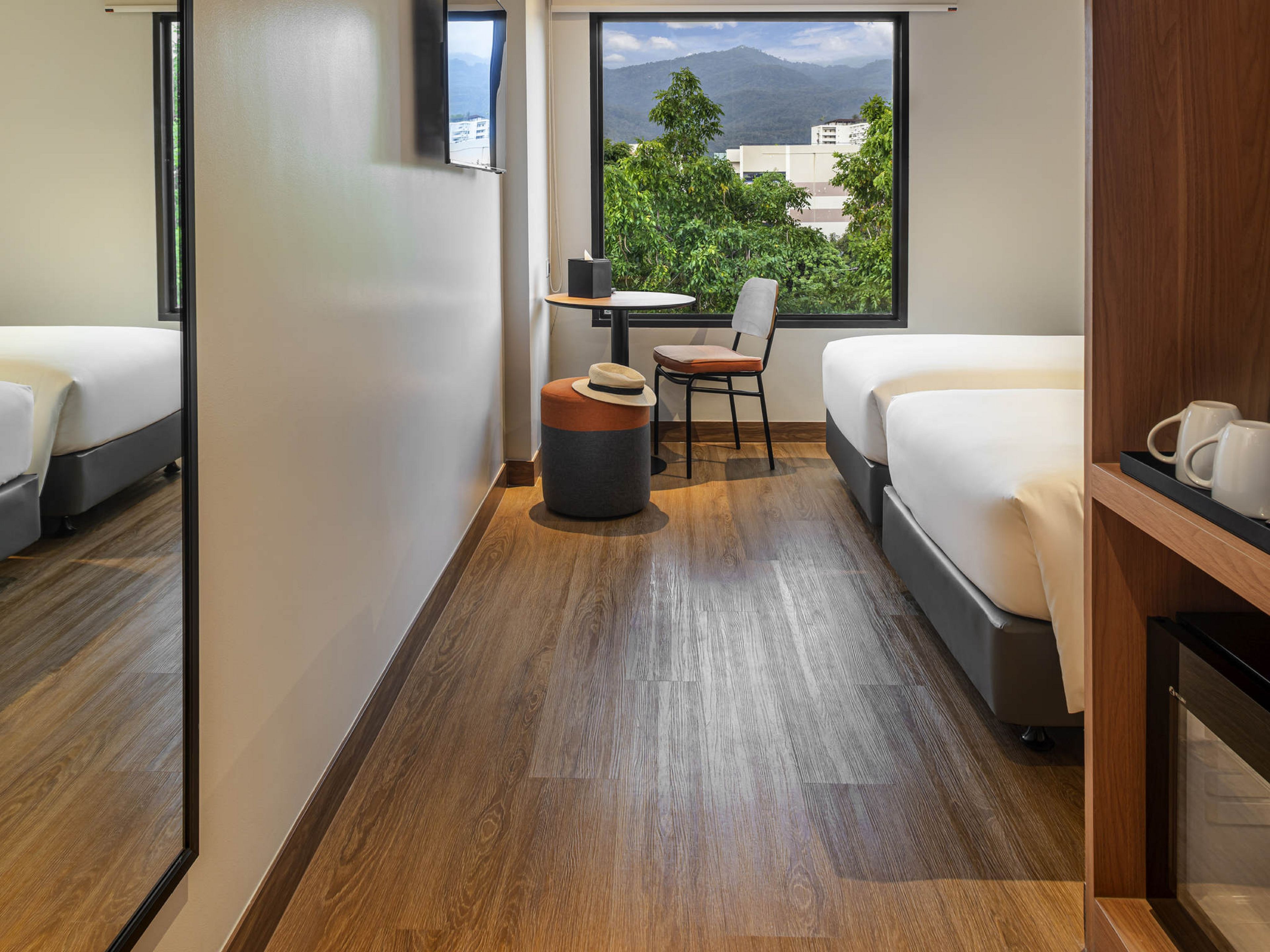 A hotel room with two beds, a small table, a chair, and a view of mountains.