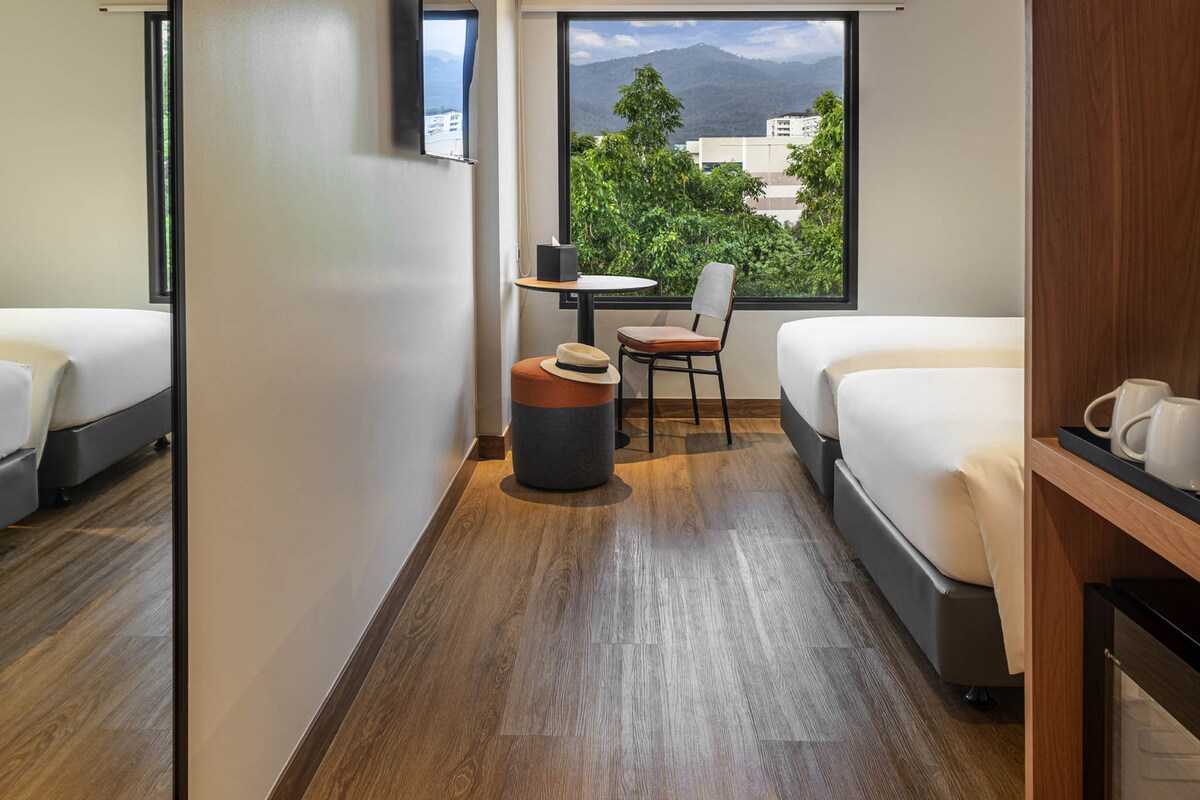 Habitación de hotel con dos camas, una mesita, una silla y vistas a las montañas.