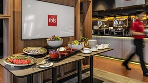 Disposição de buffet com diversos alimentos e uma tela grande exibindo o logotipo ibis.