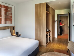 Une chambre d’hôtel avec un lit, une armoire en bois, un bureau avec une lampe et une chaise.