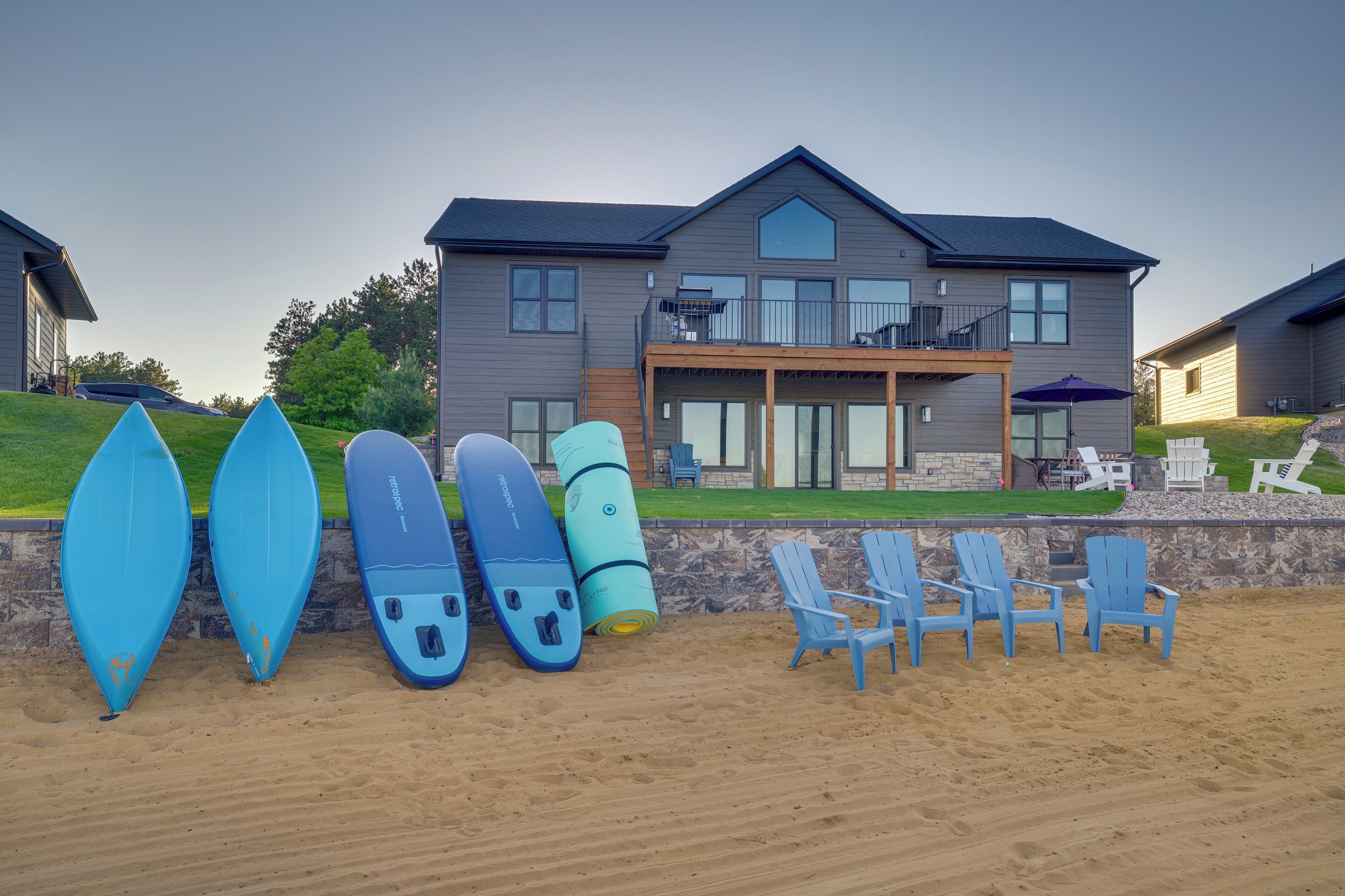 Ein Strandgrundstück mit einem großen Haus, mehreren Surfbrettern und Strandstühlen.