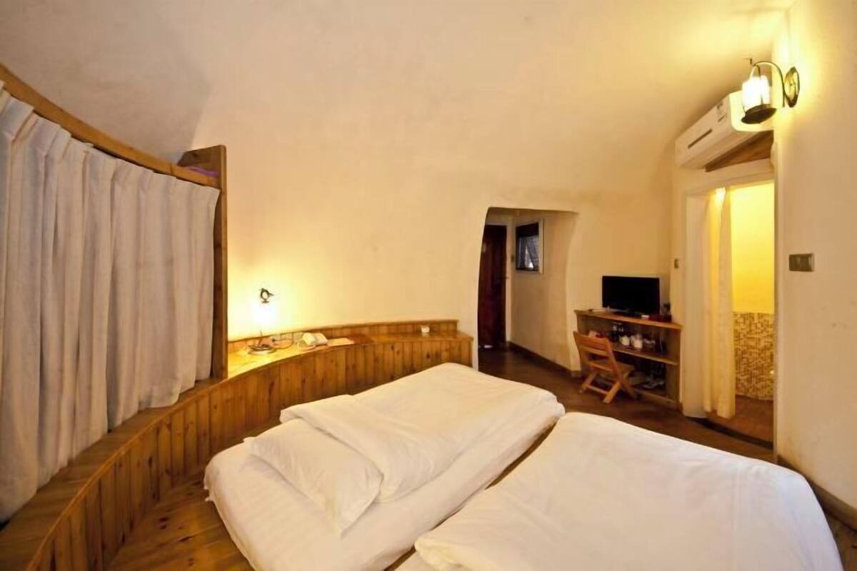 A bedroom with two beds, a wooden headboard, a desk with a chair, a television, and a wall-mounted light fixture.