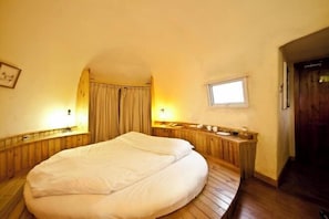 Ein Schlafzimmer mit einem Holzbett, einem kleinen Fenster und einer Holzbank mit einer Lampe.