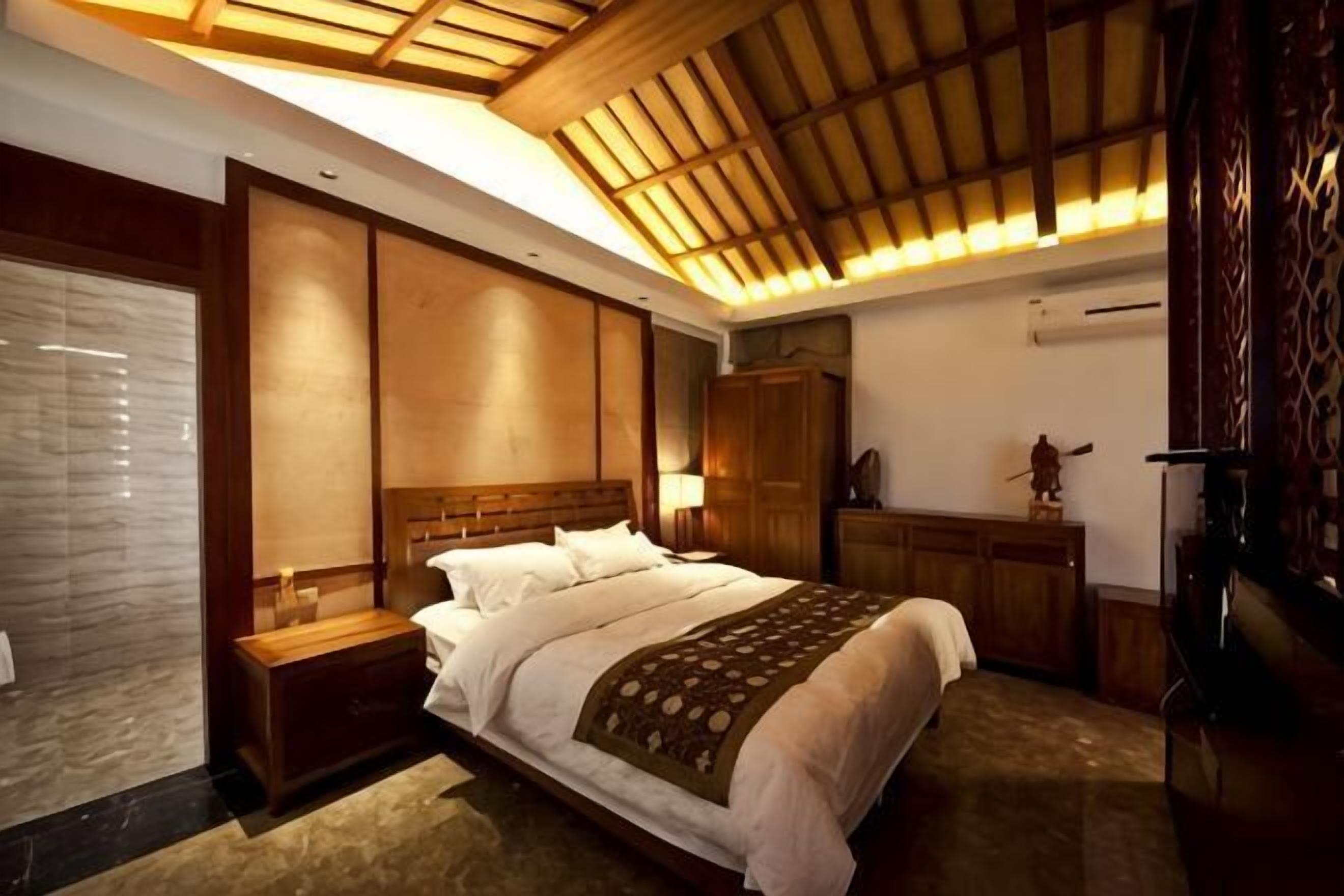 A bedroom with a large bed, wooden headboard, bedside tables, a wardrobe, and a ceiling with wooden slats.