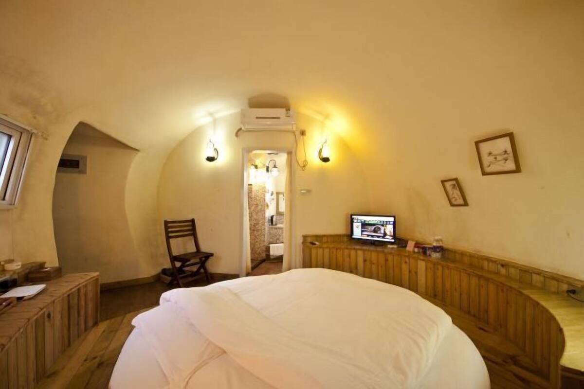 A cozy room with a large bed, wooden furniture, and a television on a wooden bench.