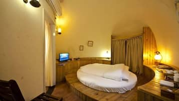 A cozy room with a curved wooden bed, a small desk with a computer, and a wooden bench.