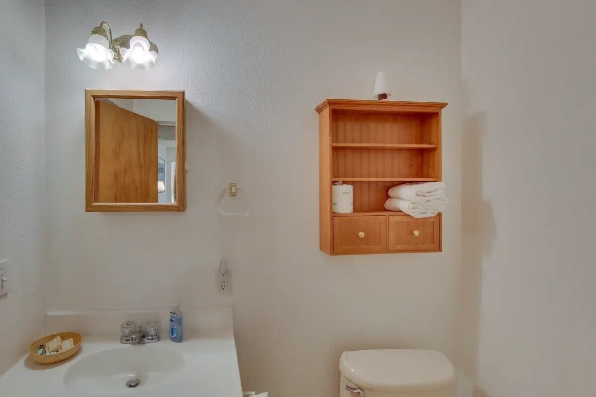 Une salle de bain avec un meuble-lavabo en bois, un miroir, une étagère avec des serviettes et des toilettes.