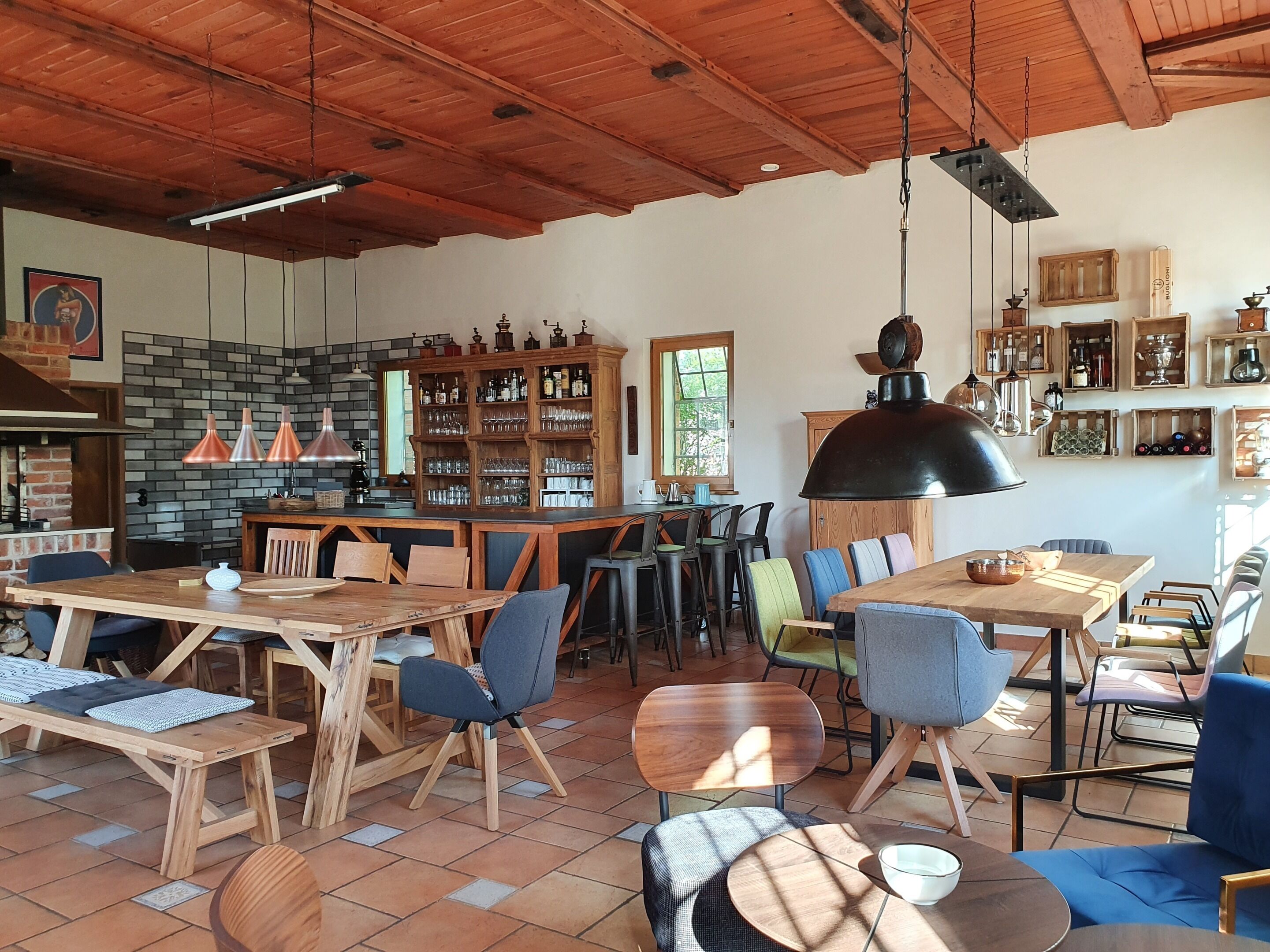 Een ruime eetruimte met houten tafels en stoelen, een bar met flessenkasten, en een hangende lamp.