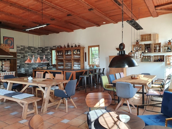 A spacious dining area with wooden tables and chairs, a bar area with shelves of bottles, and a hanging light fixture.