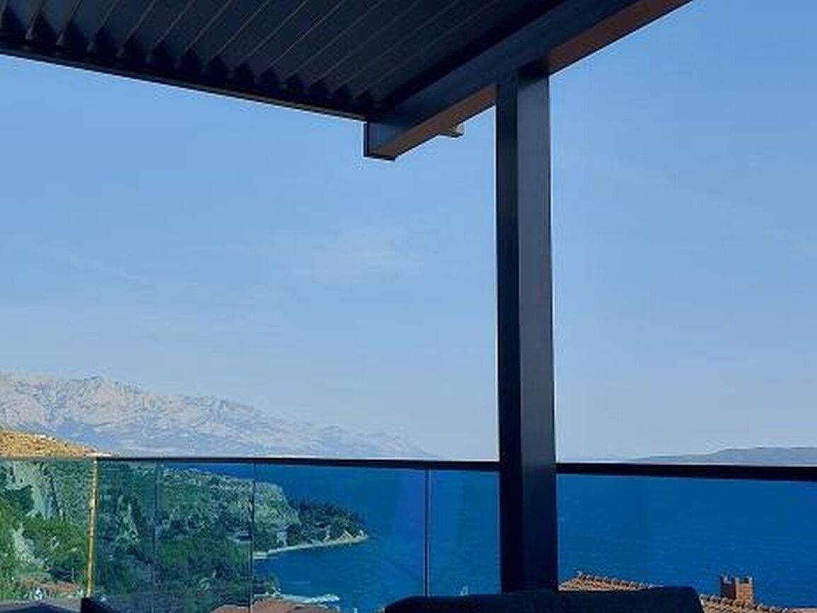 A balcony with a clear view of a coastal landscape, including a body of water and distant mountains.