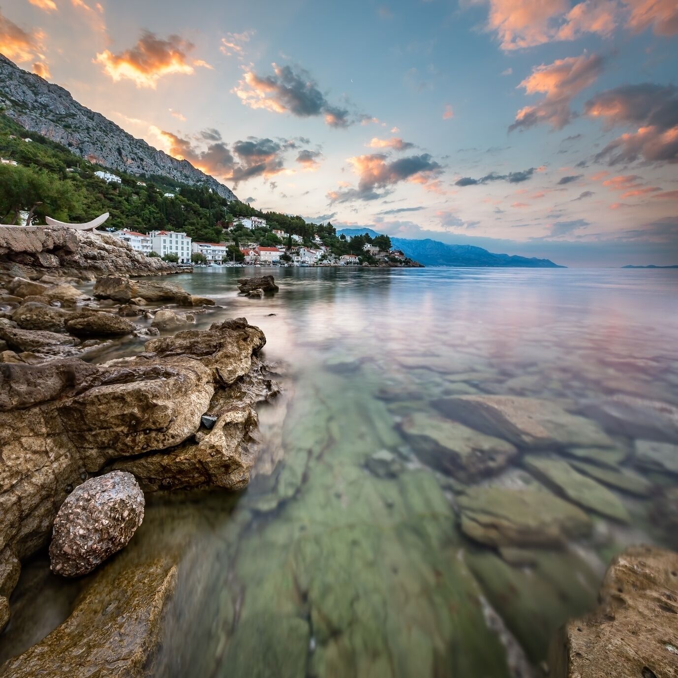 Un paysage côtier caractérisé par des rivages rocheux, une eau limpide et des bâtiments situés sur le versant d’une colline.