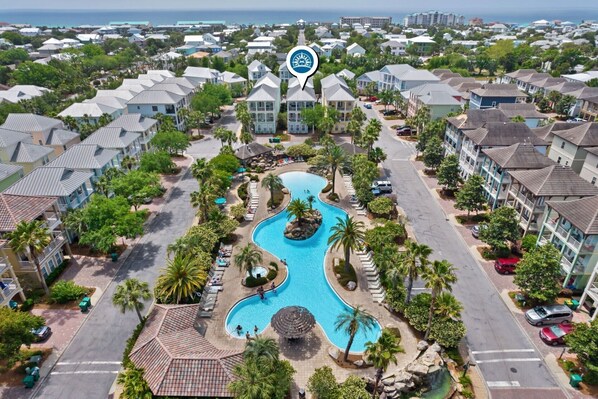 Vista aérea de un resort con una piscina central, varias edificaciones y una vista despejada del océano.