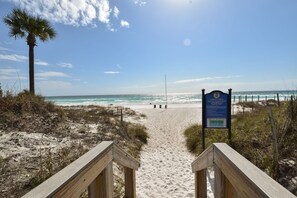 Walk along the beach pathway to the ocean, flanked by railings and a sign.