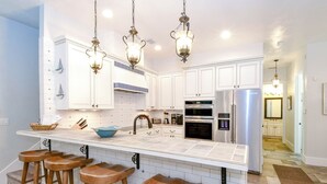 Una cocina moderna con armarios blancos, un refrigerador de acero inoxidable y una isla grande con taburetes.