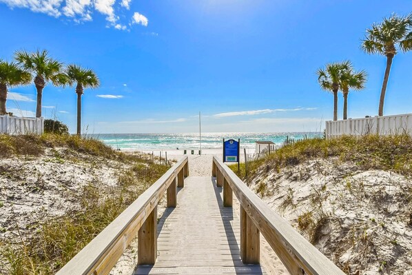 A wooden boardwalk leading to a beach with palm trees and a clear blue sky.