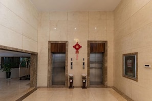 A lobby with two elevators, a red decorative hanging, and a framed sign on the wall. - Xi Feng Hotel (Pu'er)