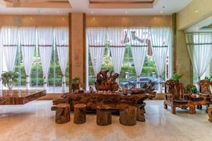 A spacious lobby with a large wooden table, several chairs, and large windows with curtains.