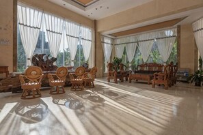 A spacious room with a large window, a wooden sofa set, and a dining table with chairs.