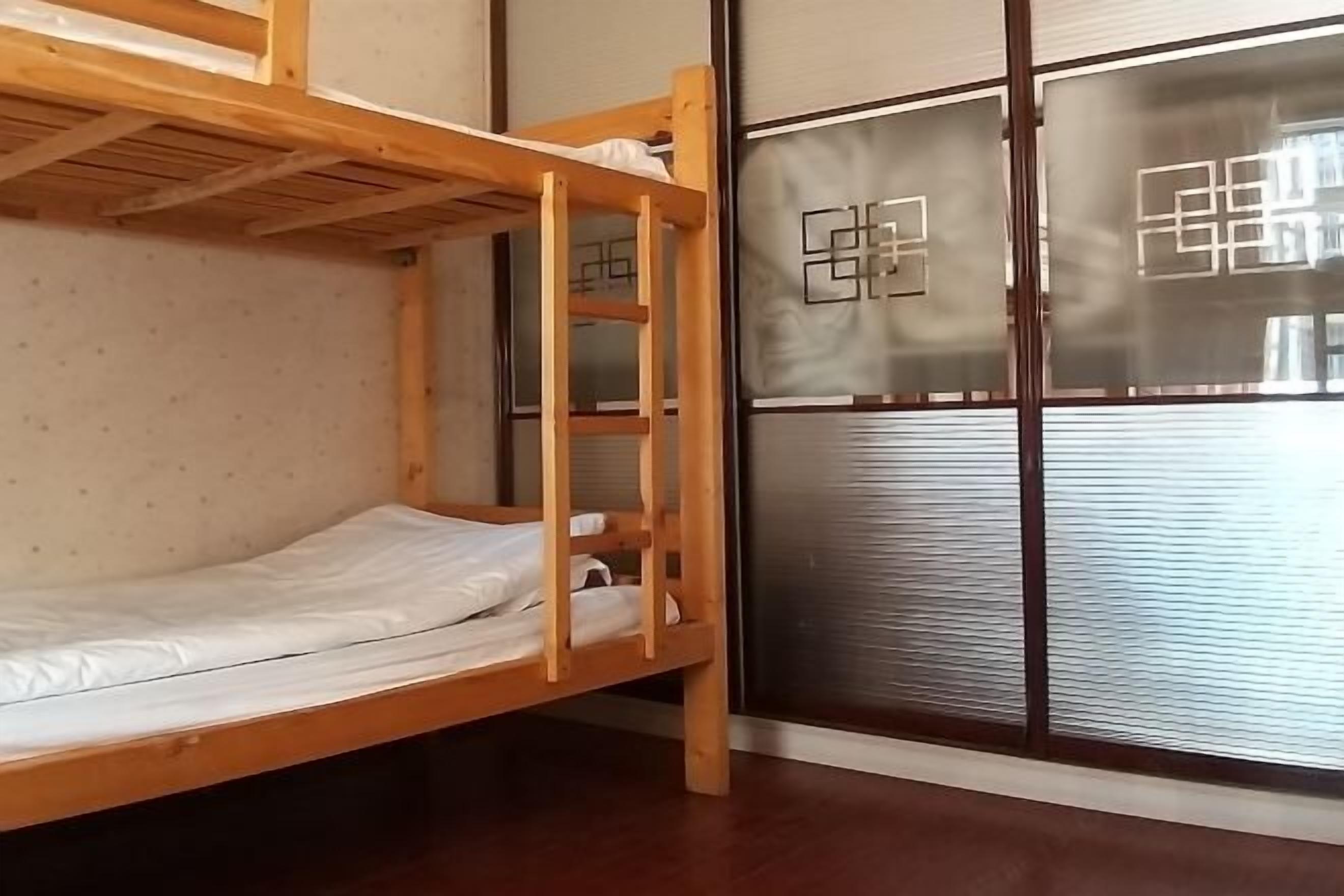 A bunk bed room with a wooden frame, a window with frosted glass, and a metal door with a geometric design.