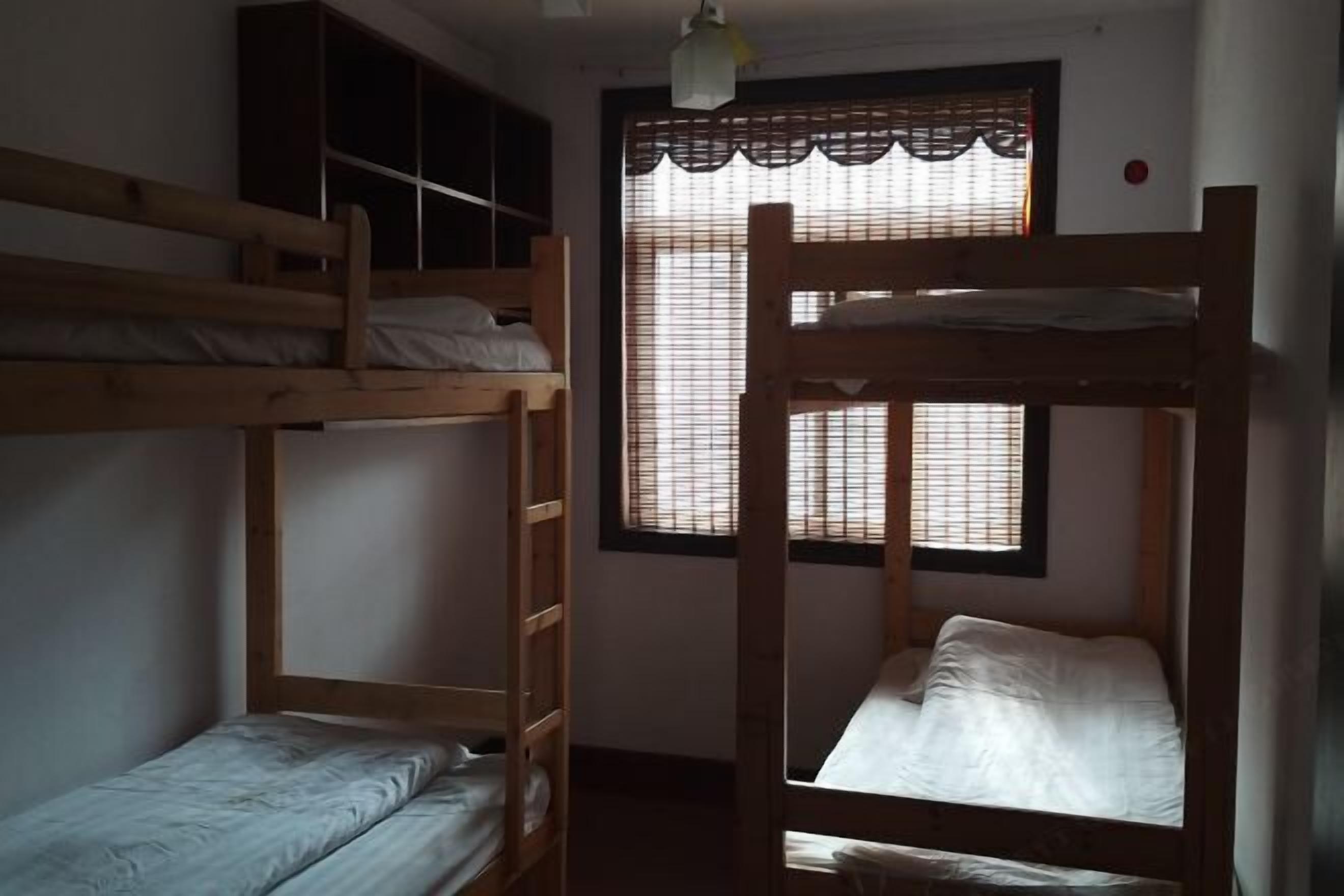 A room with two bunk beds, a window with blinds, and a ceiling light fixture.