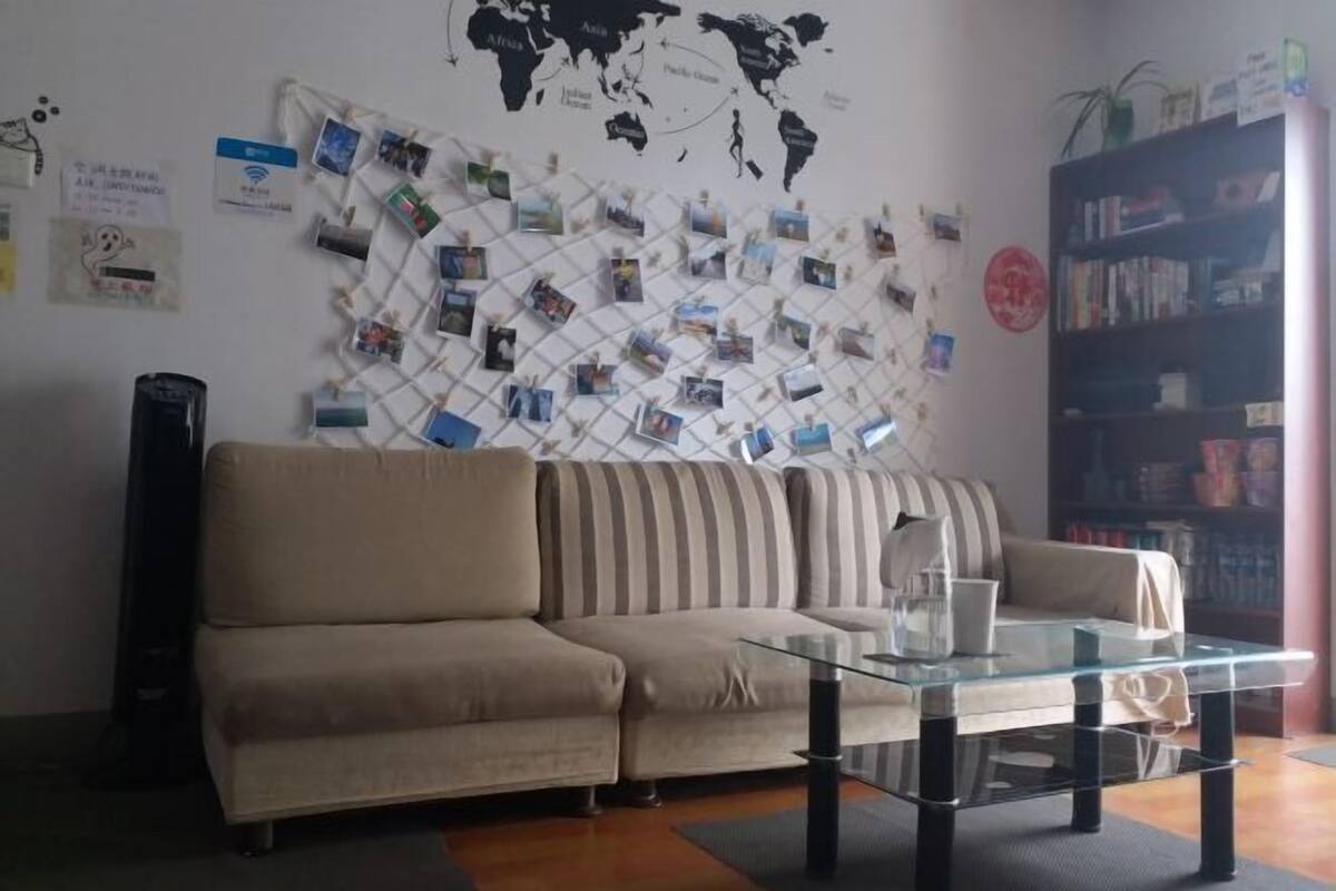 Ein Wohnzimmer mit einer Couch, einem Glastisch, einer Weltkarte an der Wand und einem Bücherregal.