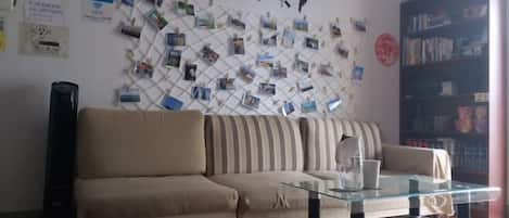 A living room with a sofa, a glass coffee table, a world map on the wall, and a bookshelf.