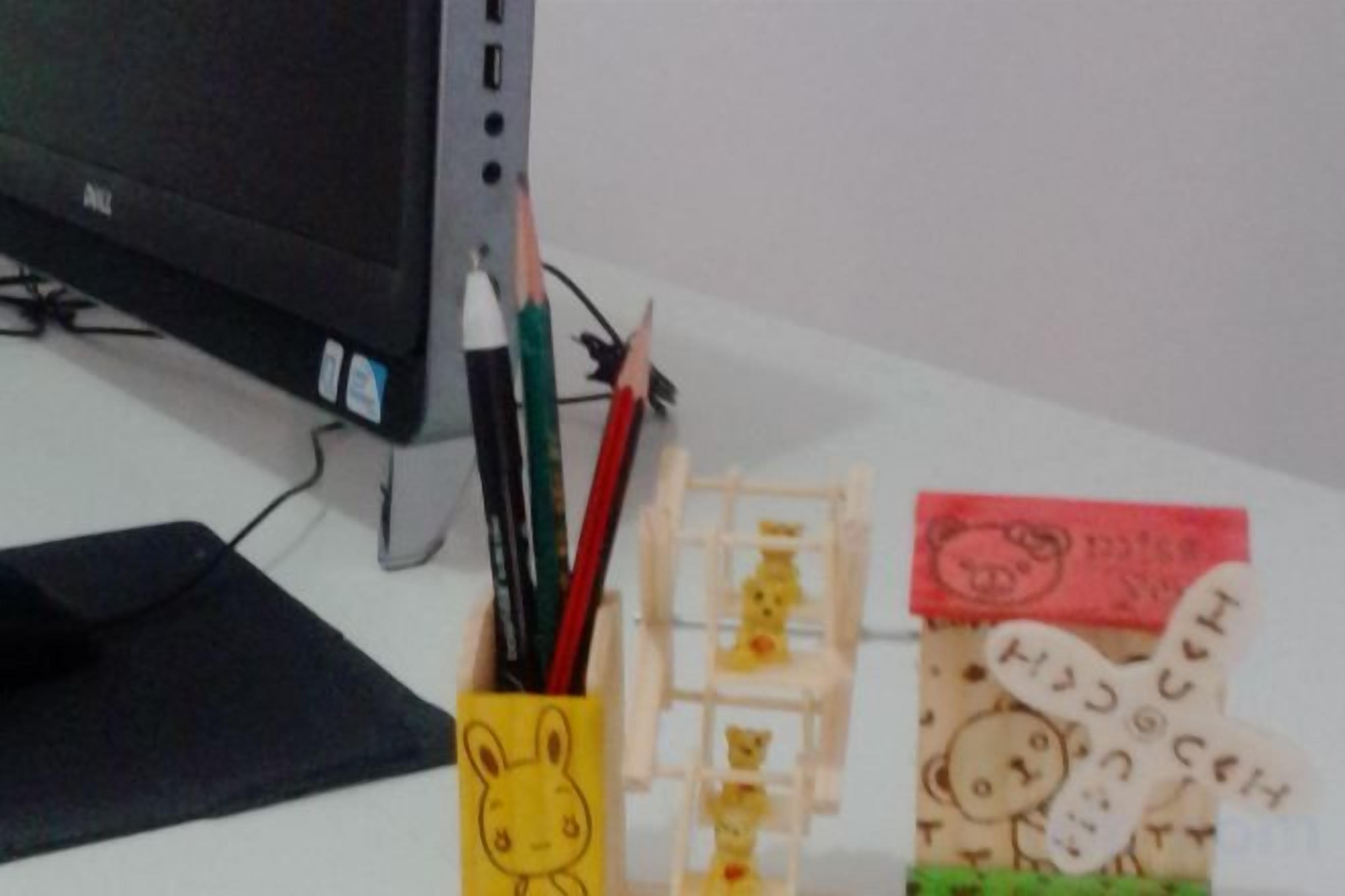 A desk with a computer monitor, a pencil holder with a cartoon character, and a small wooden structure with animal figures.