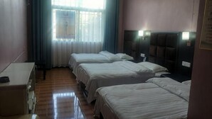Habitación de hotel con tres camas, un escritorio, una silla y un ventanal con cortinas.