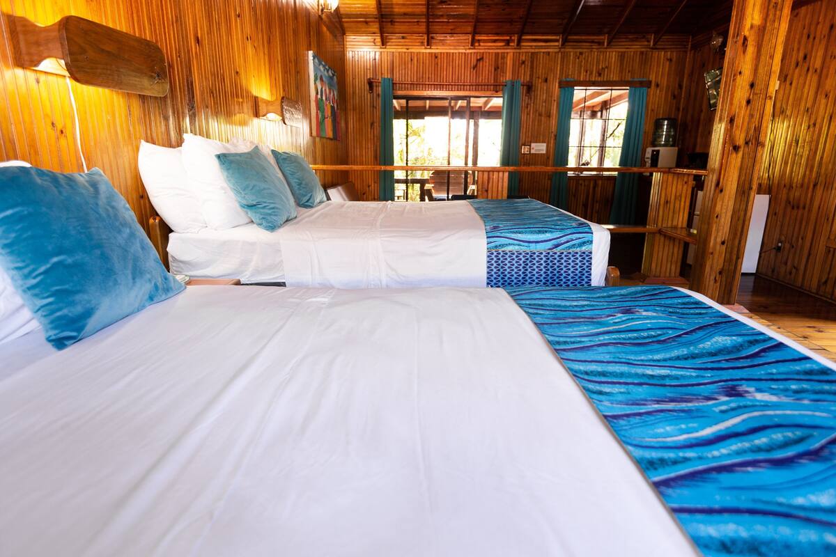 A room with two beds, wooden walls, and a view through a door.