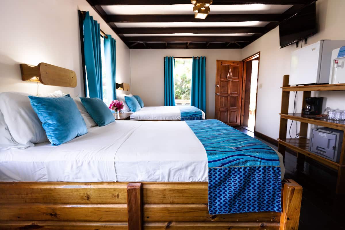 A room with two wooden beds, a wooden headboard, a shelf with a coffee maker, and a refrigerator.